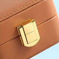 Fermoir doré sur boîte à bijoux marron en cuir avec coutures raffinées.