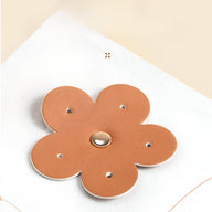 Boîte à bijoux nomade marron en forme de fleur en cuir avec bouton central doré.