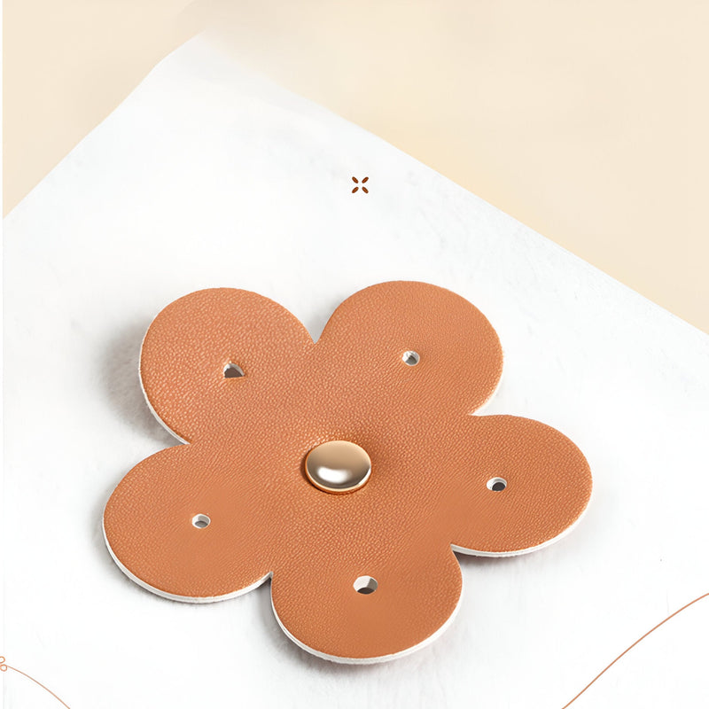 Boîte à bijoux nomade marron en forme de fleur en cuir avec bouton central doré.