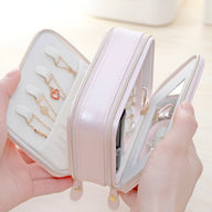 Boîte à bijoux rose nomade en cuir synthétique, double fermeture éclair, intérieur organisé avec crochets et miroir intégré.