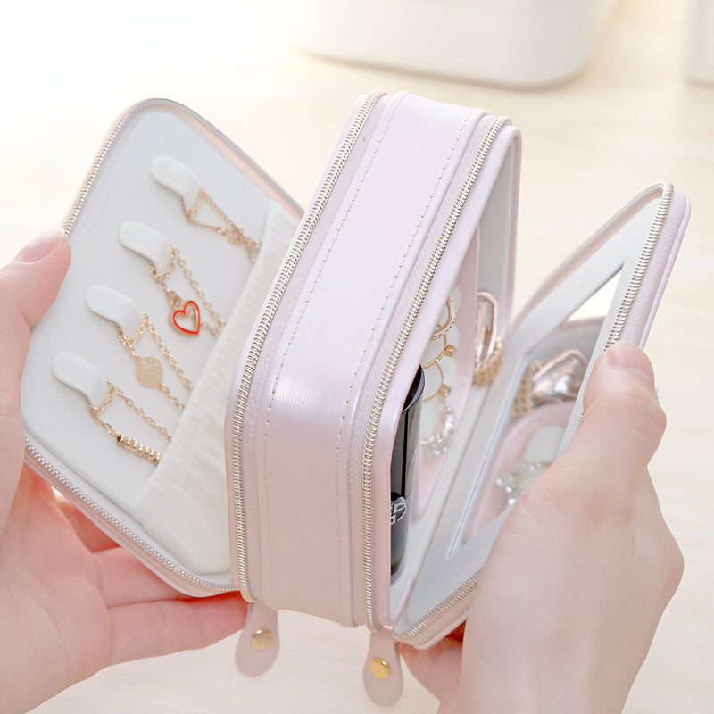 Boîte à bijoux rose nomade en cuir synthétique, double fermeture éclair, intérieur organisé avec crochets et miroir intégré.
