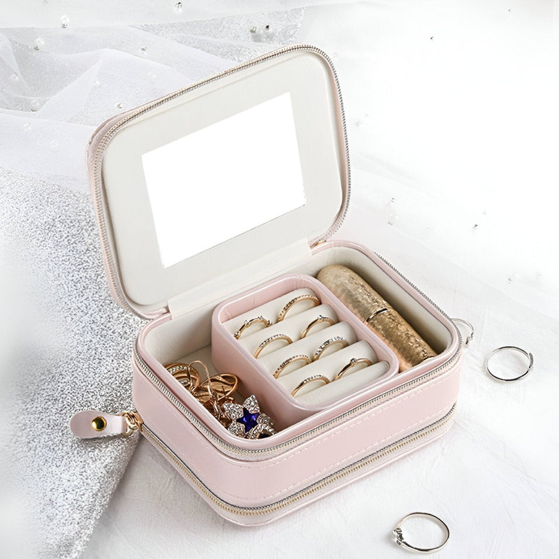 Boîte à bijoux nomade rose avec double fermeture éclair, compartiments pour bagues et accessoires, miroir intégré.