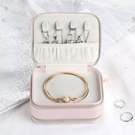 Boîte à bijoux nomade rose à double fermeture éclair avec intérieur en velours et bracelets dorés.