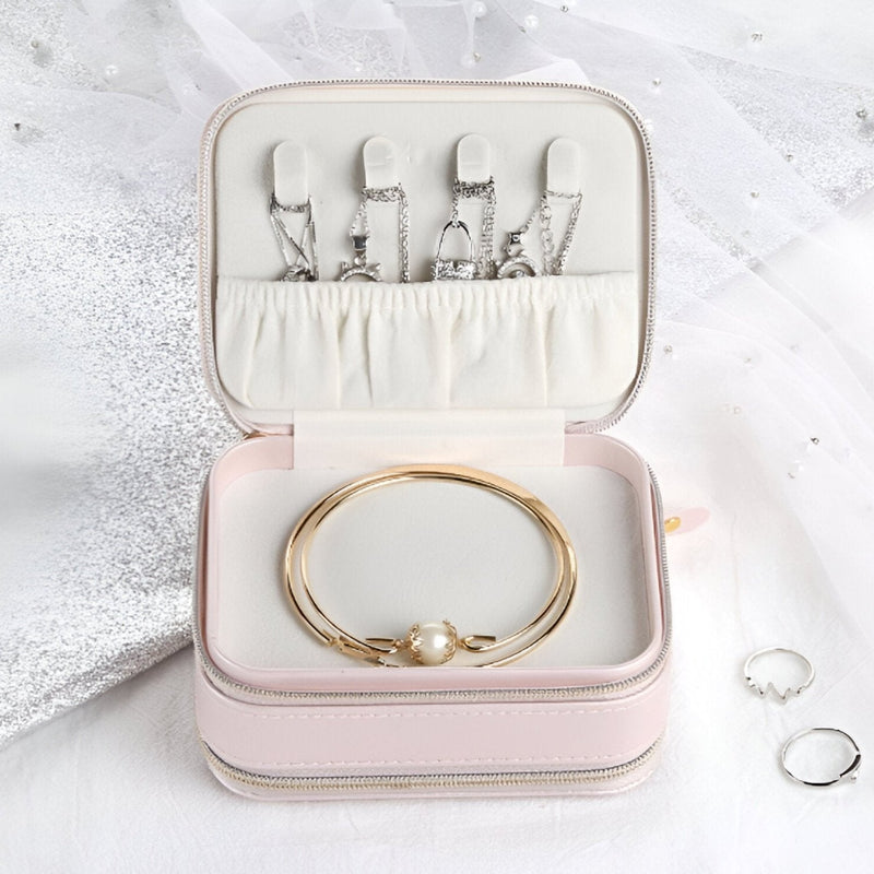 Boîte à bijoux nomade rose à double fermeture éclair avec intérieur en velours et bracelets dorés.