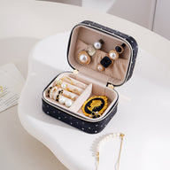 Boîte à bijoux nomade noire à strass avec compartiments pour bagues et boucles d’oreilles, intérieur beige doux.