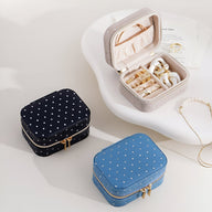 Trois boîtes à bijoux nomades avec strass, en beige ouvert, bleu et noir fermés, fermetures éclairs dorées.