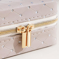 Boîte à bijoux beige matelassée avec strass, fermeture éclair or double curseur raffinée.