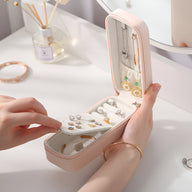 Boîte à bijoux nomade allongée rose en cuir avec rangements pour boucles d’oreilles et colliers.
