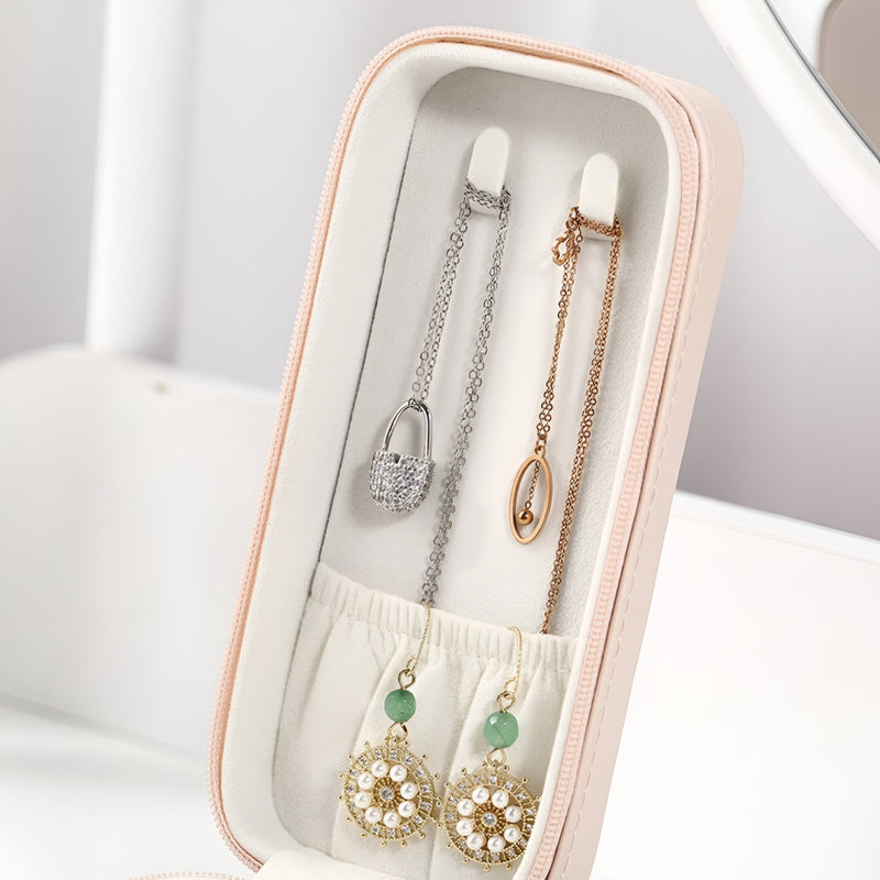 Boîte à bijoux nomade allongée rose avec compartiments pour colliers et boucles d’oreilles.