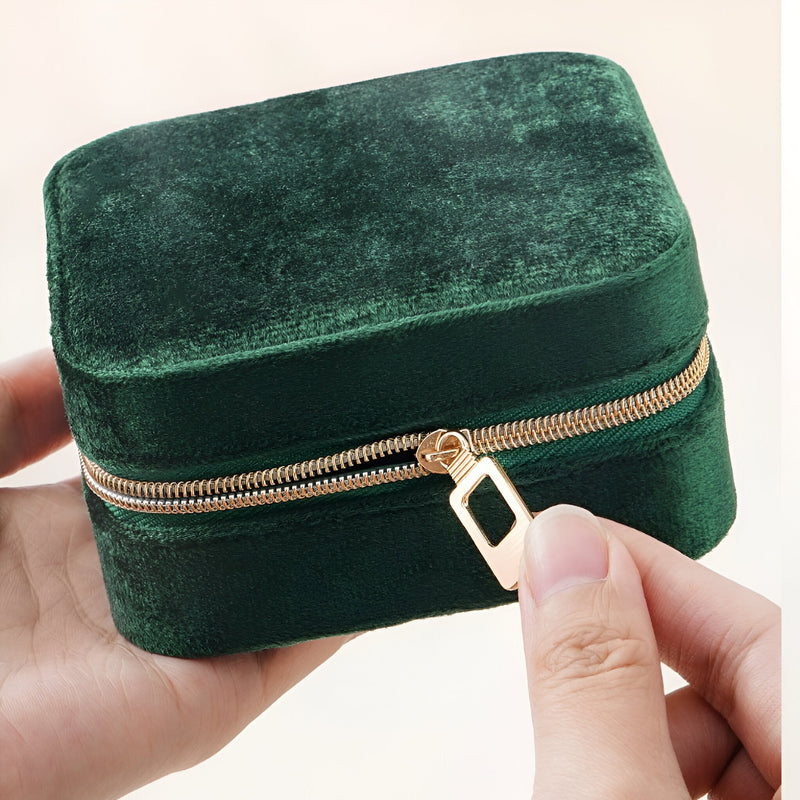 Boîte à bijoux nomade en velours vert foncé avec fermeture éclair dorée tenue en main.
