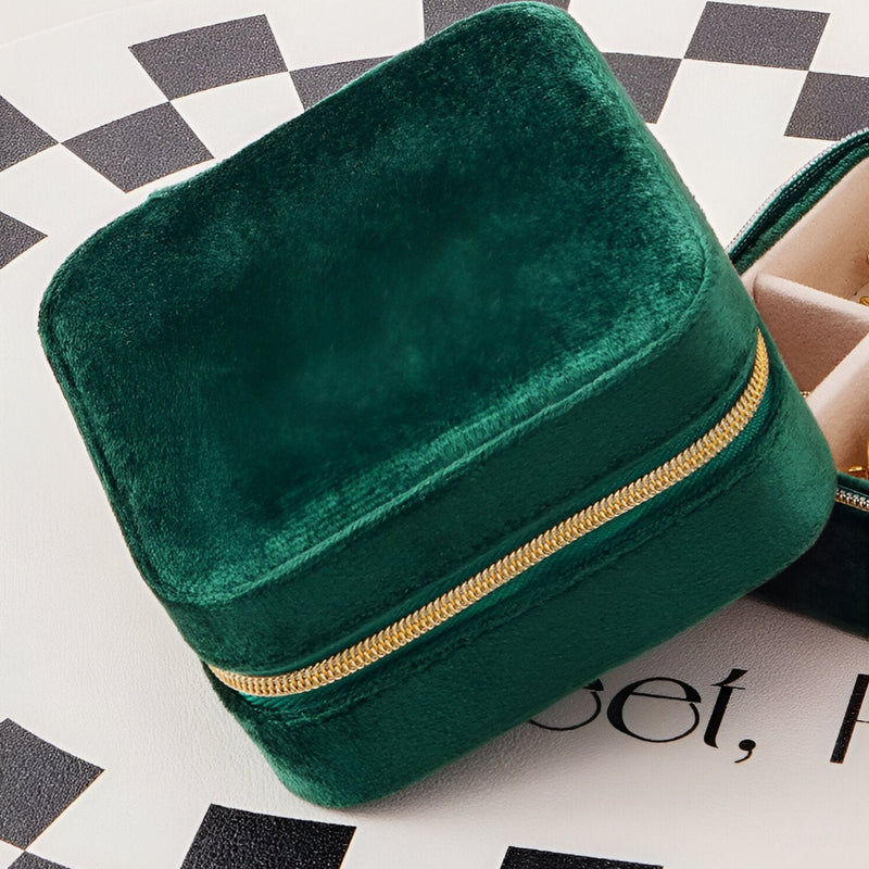 Boîte à bijoux nomade carrée en velours vert avec fermeture éclair dorée.