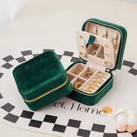 Boîte à bijoux nomade en velours vert foncé avec intérieur beige, miroir et compartiments pour bagues et boucles d’oreilles.
