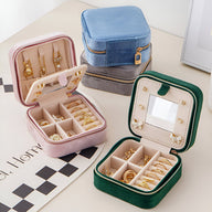 Boîte à bijoux nomade en velours rose avec compartiments et anneaux pour bagues, ouverture zip.