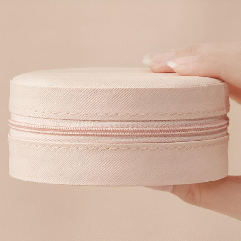 Boîte à bijoux ronde nomade rose pâle en cuir avec fermeture éclair, tenue à la main.