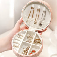 Boîte à bijoux ronde rose avec compartiments et crochets pour colliers, design élégant et compact.