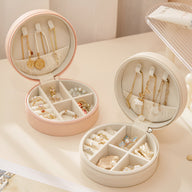 Boîtes à bijoux nomades rondes en cuir rose et blanc avec compartiments et crochets pour colliers.