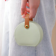Boîte à bijoux nomade ronde vert clair avec anse en cuir camel et bouton doré.
