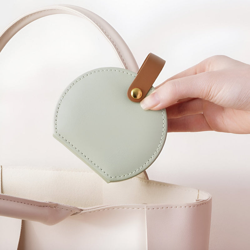 Boîte à bijoux nomade ronde verte en cuir avec fermeture pression et couture visible.