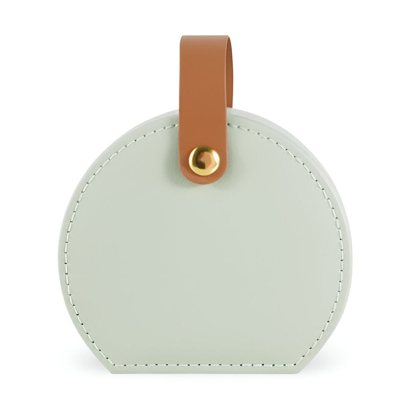 Boîte à bijoux nomade ronde en cuir vert pâle avec anse marron en cuir et bouton doré.