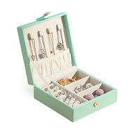 Boîte à bijoux nomade carrée bleue avec compartiments multiples et crochets pour colliers, fermeture bouton doré.