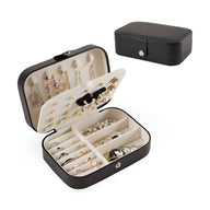 Boîte à bijoux nomade noire en cuir, compartiments multiples avec coussins pour bagues et crochets pour boucles d'oreilles.