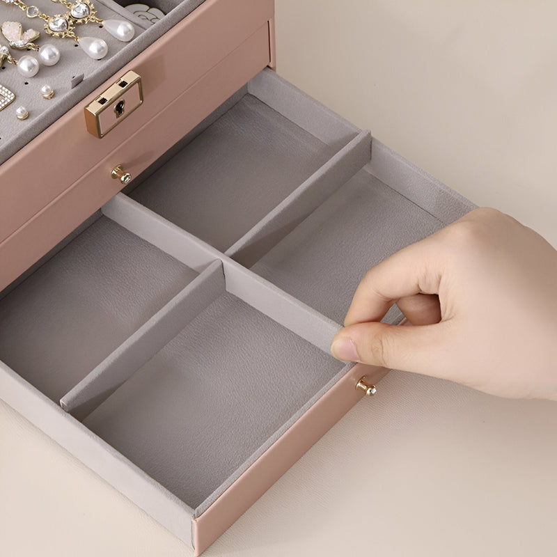 Boîte à bijoux rose grand format avec compartiments doublés de velours et fermeture dorée.