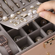 Boîte à bijoux beige avec tiroirs modulables et compartiments pour bagues, colliers et montres, main retirant une bague en.