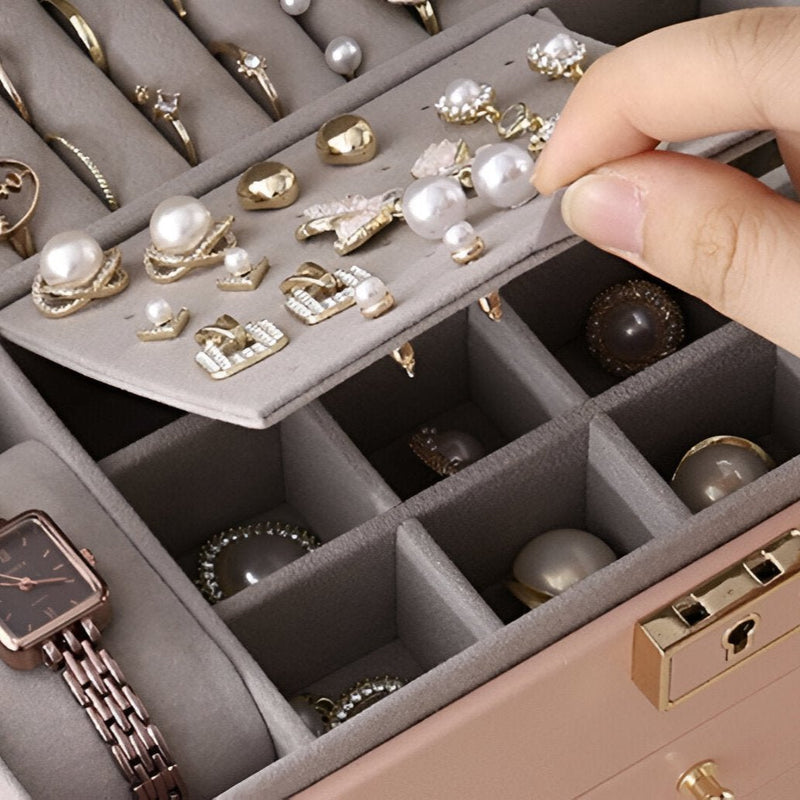 Boîte à bijoux beige avec tiroirs modulables et compartiments pour bagues, colliers et montres, main retirant une bague en.