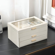 Boîte à bijoux blanche grand format avec tiroirs et couvercle en verre, poignées or rose.