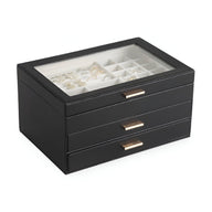 Boîte à bijoux noire grand format avec couvercle transparent et trois tiroirs à poignées dorées.