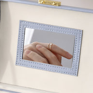 Miroir rectangulaire encadré de cuir blanc avec surpiqûres décoratives sur boîte à bijoux.