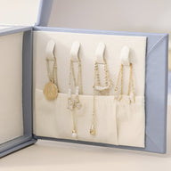 Boîte à bijoux bleue ouverte avec compartiments organisant colliers et pendentifs sur fond beige.