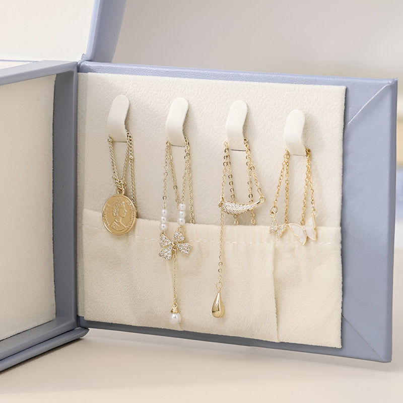 Boîte à bijoux bleue ouverte avec compartiments organisant colliers et pendentifs sur fond beige.