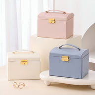 Boîtes à bijoux nomades en cuir rose pâle, bleu et crème avec poignée et fermoir doré.