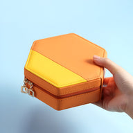 Boîte à bijoux hexagonale bi-colore orange et jaune avec fermeture éclair dorée, tenue en main.