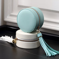 Boîte à bijoux ronde bleue avec pompon et fermeture éclair, posée sur boîte blanche similaire.