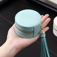 Boîte à bijoux ronde bleu clair en cuir avec pompon attaché sur une main.