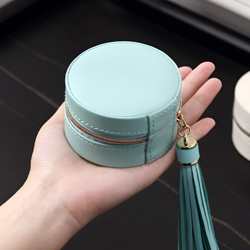 Boîte à bijoux ronde bleu clair en cuir avec pompon attaché sur une main.