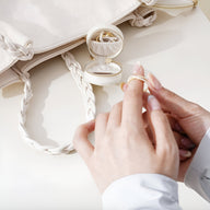 Boîte à bijoux nomade blanche ronde ouverte avec anneau, pose main féminine retirant bague délicate.