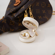 Boîte à bijoux nomade mini format blanche ouverte avec boucles d’oreilles en perles et or, posée devant un sac en cuir.