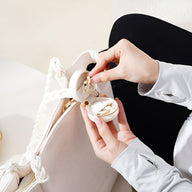 Mini boîte à bijoux nomade ronde blanche avec intérieur en velours, portée à la main.