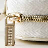 Glossy gold zipper pull with textured detail on white textured fabric jewelry box.