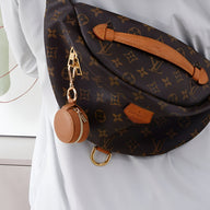 Sac banane en toile monogrammée marron avec petite boîte à bijoux ronde en cuir marron attachée.