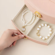 Boîte à bijoux nomade rose avec miroir, intérieur beige, bracelet et collier perles blancs, fermoir doré.