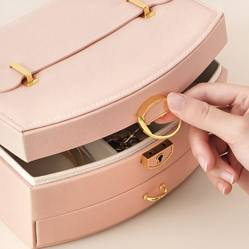 Boîte à bijoux rose avec miroir intégré, fermeture ronde dorée, cuir lisse et élégante poignée dorée.