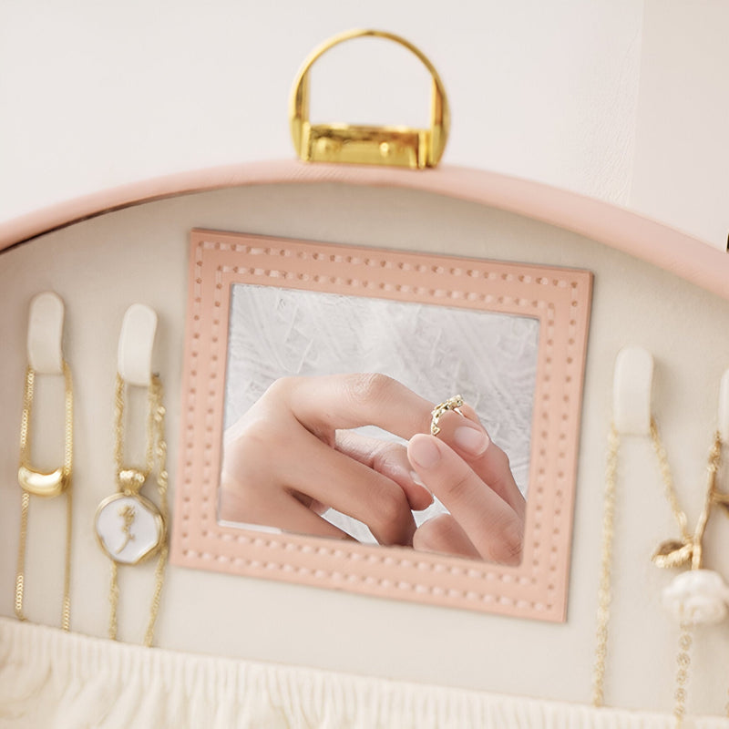 Boîte à bijoux rose avec miroir carré intégré et plusieurs compartiments pour chaînes et montres.