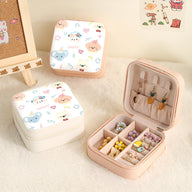 Boîte à bijoux nomade rose ouverte avec compartiments et crochets, motifs animaux colorés sur la boîte blanche fermée.