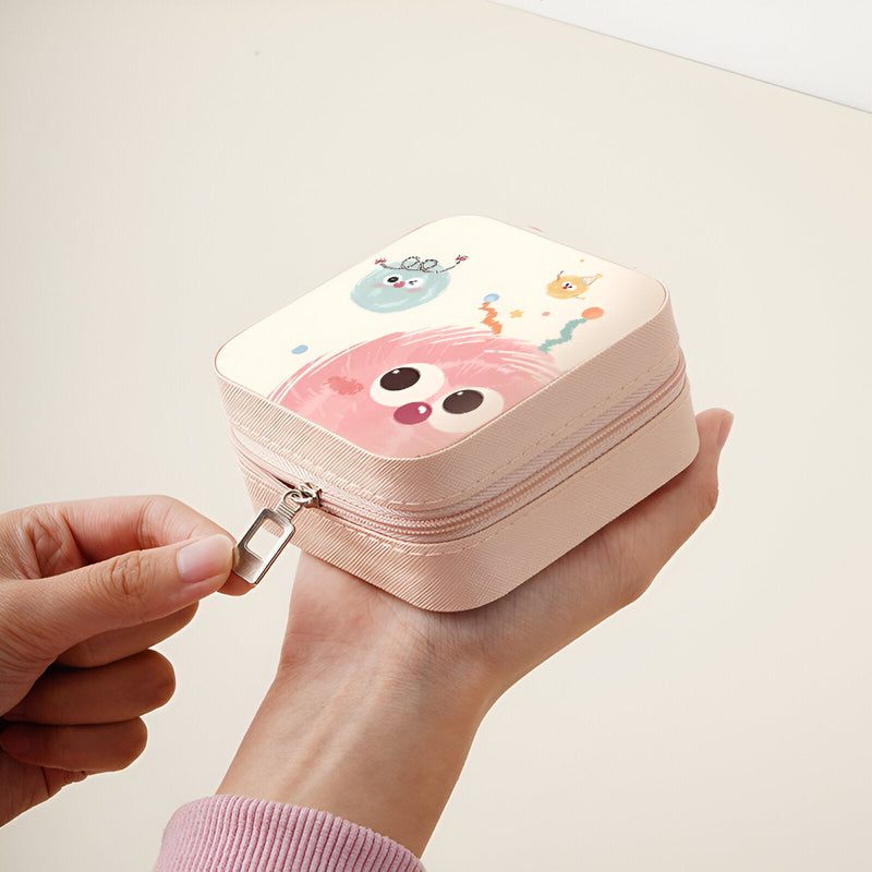 Boîte à bijoux rose compacte avec motif monstres colorés et fermeture éclair métallique.