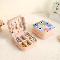 Boîte à bijoux rose nomade ouverte avec compartiments et motifs monstres colorés sur le couvercle fermé.