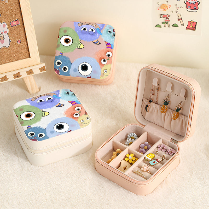 Boîte à bijoux nomade rose ouverte avec compartiments et crochets, motif monstres colorés playful.